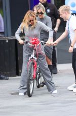 AMANDA HOLDEN and ASHLEY ROBERTS Ride a Tandem Bike at Leicester Square in London 10/03/2024